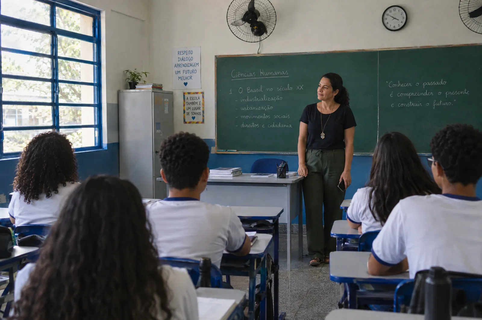 Professora em frente ao quadro, com os alunos sentados de frente para ela